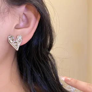 Detailed close-up of a silver-toned hammered heart stud earring worn on an earlobe