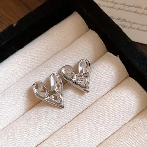 Macro view of silver metallic heart earrings with a textured molten surface in a tray.