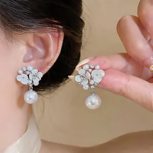 Close-up of elegant white flower earrings with drop pearls and sparkling rhinestones