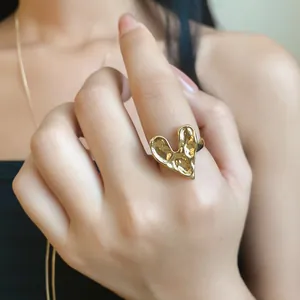 Close-up of a minimalist gold textured heart ring worn on a finger.