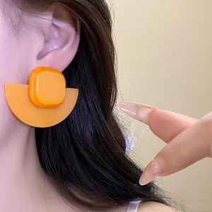 Macro view of bright orange resin geometric stud earrings on the ear of a model