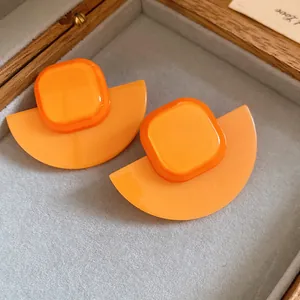 Macro view of vibrant orange resin geometric fan-shaped stud earrings in a jewelry box