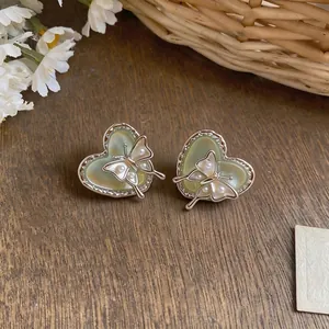 Sweet heart shaped stud earrings with butterfly and pearl accents on wooden background