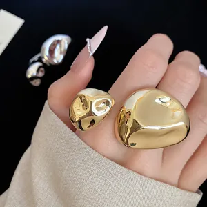 Dettaglio di un anello aperto dorato irregolare con una trama liscia effetto fuso.