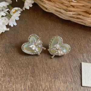 Close-up of heart-shaped earrings with butterfly pearl details on wooden background