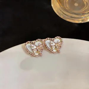 Close-up detail of golden butterfly and pearl heart stud earrings on a white plate