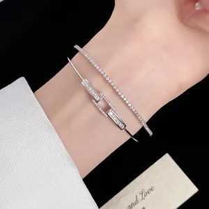 Macro detail of silver plated zircon interlocking square open bangle and tennis bracelet on wrist
