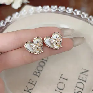 Close-up of elegant heart-shaped pearl stud earrings with delicate butterfly design detail.