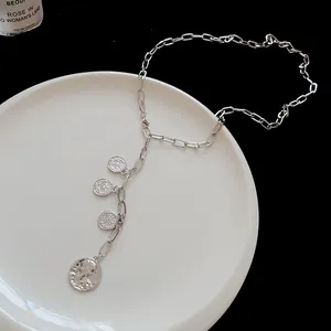 Macro detail of a silver Y-shape necklace with four round portrait coin pendants.