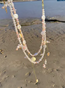 Detailed view of a gold-toned body chain with white pearls and pink shell accents.