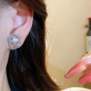 Detailed view of 14k gold plated flower stud earrings with a central pearl on a model