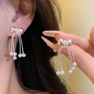 Close-up of elegant bow stud earrings with delicate pearl tassels and silver finish