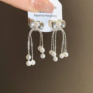 Close-up of elegant silver bow-knot earrings with delicate hanging white pearl tassels