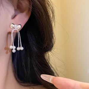 Detailed view of silver bow stud earrings featuring elegant pearl tassels on a model's ear