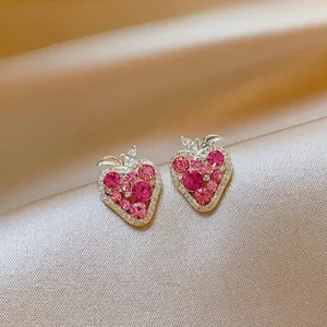 Detailed view of pink zircon strawberry stud earrings on champagne satin background