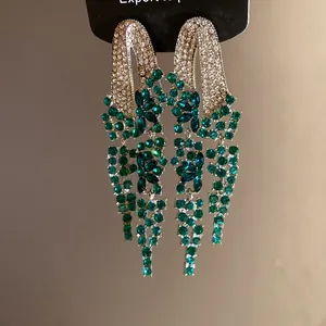 Detailed macro view of silver needle tassel earrings with green and white rhinestones