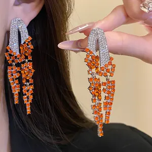Detailed view of silver needle tassel earrings with orange and clear rhinestones