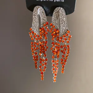 Close-up of elegant silver needle earrings with orange stones and diamond tassel
