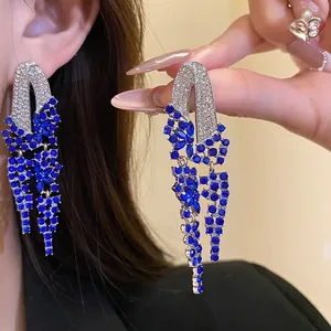 Detail of elegant silver needle earrings with blue rhinestone geometric tassels.