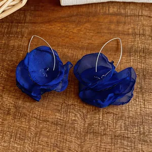 Nahaufnahme von tiefblauen Chiffon-Blumenohrringen mit eleganten silbernen Haken auf Holz.