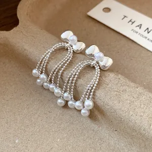 Detailed macro view of elegant silver bow stud earrings featuring delicate pearl bead tassels