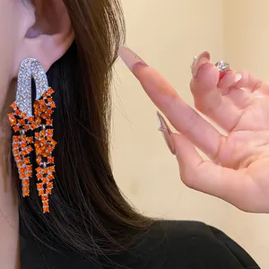 Detail of elegant silver tassel earrings with orange rhinestones on model's ear