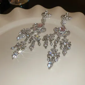 Close-up shot of sparkling rhinestone tassel heart earrings displayed on a wavy ceramic plate.