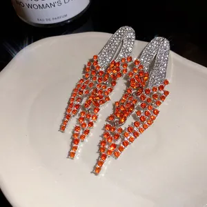 Close-up detail of luxury geometric tassel earrings with brilliant orange rhinestones