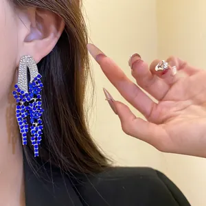Detail view of silver geometric tassel earrings with vibrant blue crystals on model.
