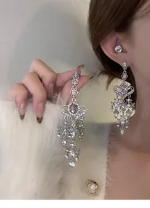 Close-up of elegant silver tassel earrings with a pink heart-shaped stone on a model.