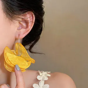 Nahaufnahme eleganter großer gelber Chiffon-Blumen-Ohrhänger an einem weiblichen Ohr.