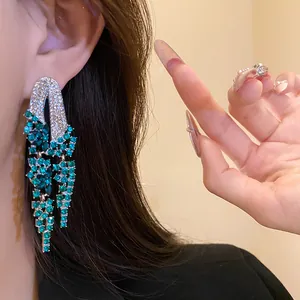 Close-up of elegant green and silver rhinestone geometric tassel earrings worn by a model.