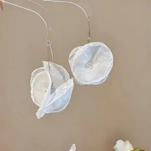 Detailansicht eleganter weißer Chiffon-Blumenohrringe an einem klaren Präsentationsständer