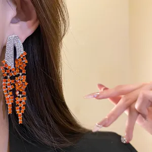 Detailed close-up of glamorous orange rhinestone tassel earrings worn by a model.