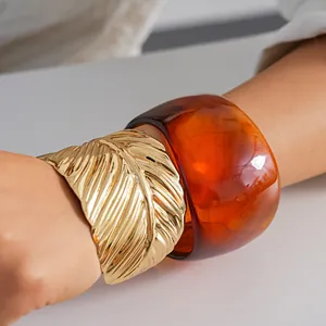 Detail view of chunky amber resin bangle and gold textured metal cuff bracelet