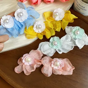 Close-up of colorful chiffon flower pearl earrings on a wooden tray background