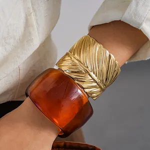 Detailed shot of an amber resin bangle paired with a textured gold metal leaf cuff on a wrist.