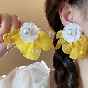 Detailed shot of oversized yellow chiffon flower earrings with white pearl center decoration