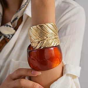 Close-up of wide gold feather textured cuff and thick amber resin bangle on wrist.