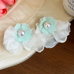 Macro view showing delicate mint green chiffon flower and pearl detail on white earrings