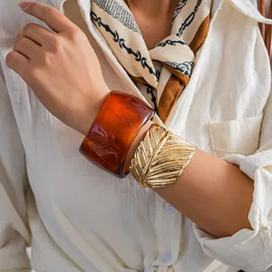Detail of chunky amber resin geometric bangle paired with a gold leaf metal cuff on arm