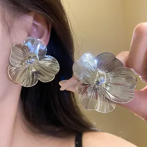 Close-up of elegant silver-toned brushed metal flower earrings with central pearl detail.