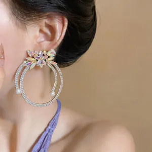 Exaggerated gold-toned rhinestone hoop earrings with flower and pearls detail on model