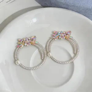 Close-up of luxury rhinestone hoop earrings with iridescent floral motif and pearl