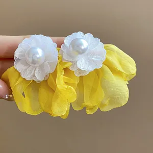 Detailed view of yellow chiffon flower earrings with white fabric petals and central pearl.