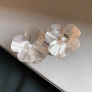 Detail shot of silver brushed metal flower ear clips with a white pearl center point.