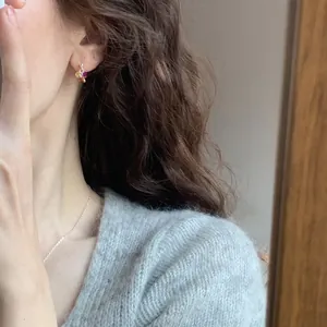Detail shot of colorful zircon stud earrings worn by a model with a gray sweater.