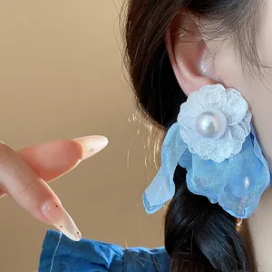 Close-up of blue and white chiffon flower pearl stud earrings worn on model ear