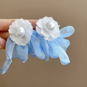Close-up detail of elegant light blue chiffon flower and pearl earrings with white lace