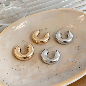 Macro detail of minimalist gold and silver C-shaped chunky hoop earrings on ceramic plate